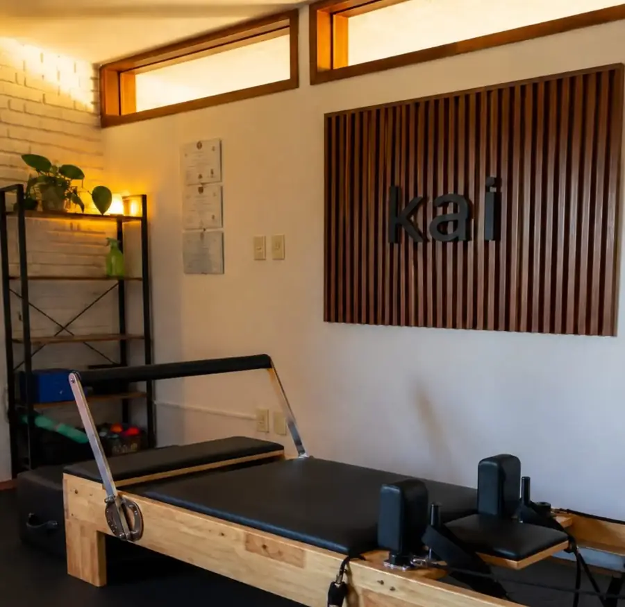 La sala de Pilates Estudio de Kai: un reformer de madera clara frente al cartel de kai sobre listones de madera, con luz cálida