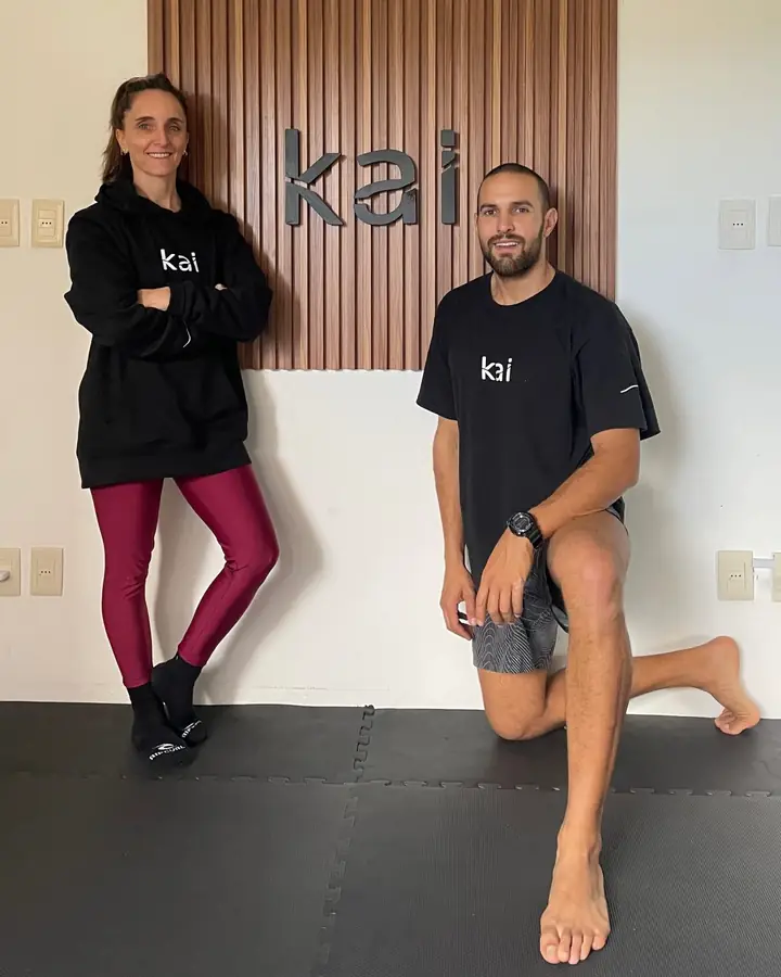 Euge y Rodri, de negro y con remeras de kai, frente a los listones de madera con el cartel de kai