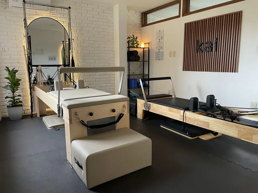 La sala de reformer: un reformer con media torre, otro reformer, el espejo en arco con luz cálida y el cartel de kai