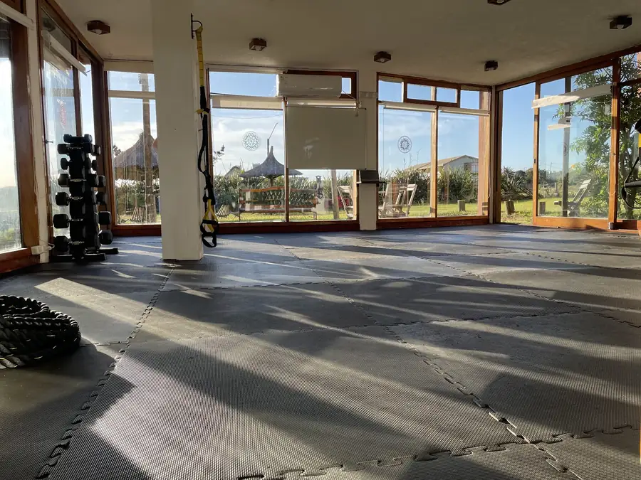 La sala principal con el sol de la tarde y, detrás de los ventanales, el jardín con sombrillas de paja