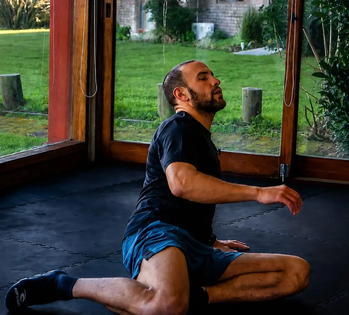 Movimiento natural en la sala vidriada de Kai: un hombre se mueve sobre el piso de goma con el jardín verde detrás de los ventanales
