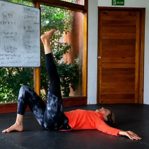 Sofía, alumna de Kai, hace un ejercicio en el piso con una pierna arriba, junto a la pizarra y los ventanales